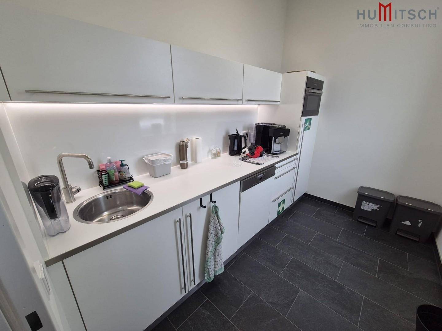 Moderne Einbauküche mit weißen Schränken, Spüle und dunklem Fliesenboden.