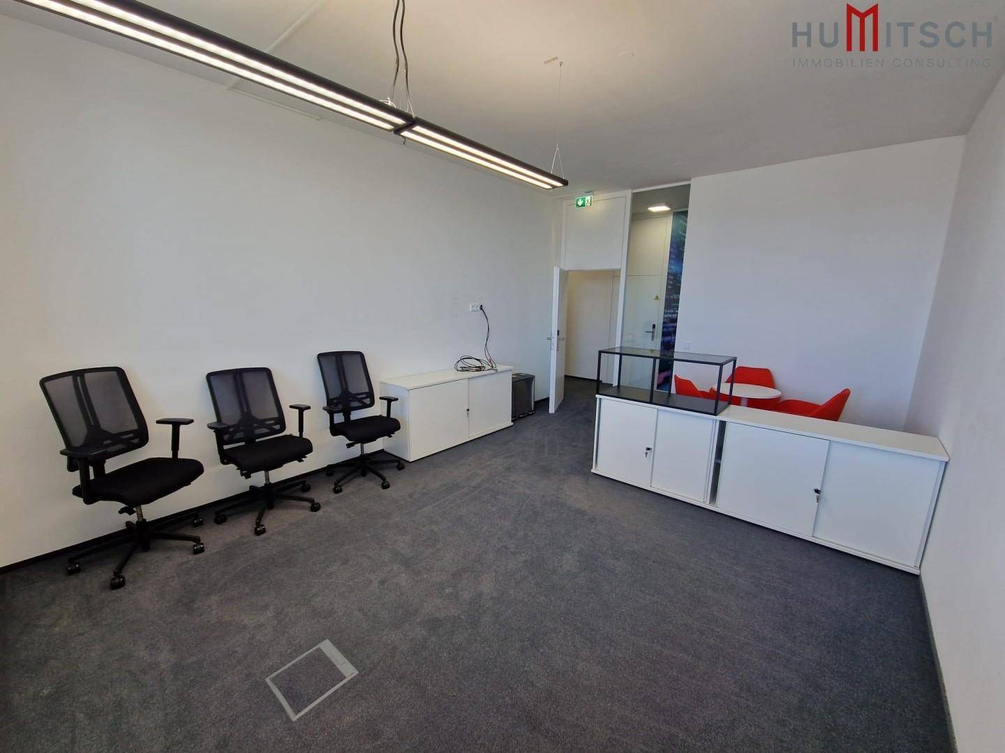 Moderner Bürobereich mit Teppichboden, weißen Schränken und ergonomischen Bürostühlen.