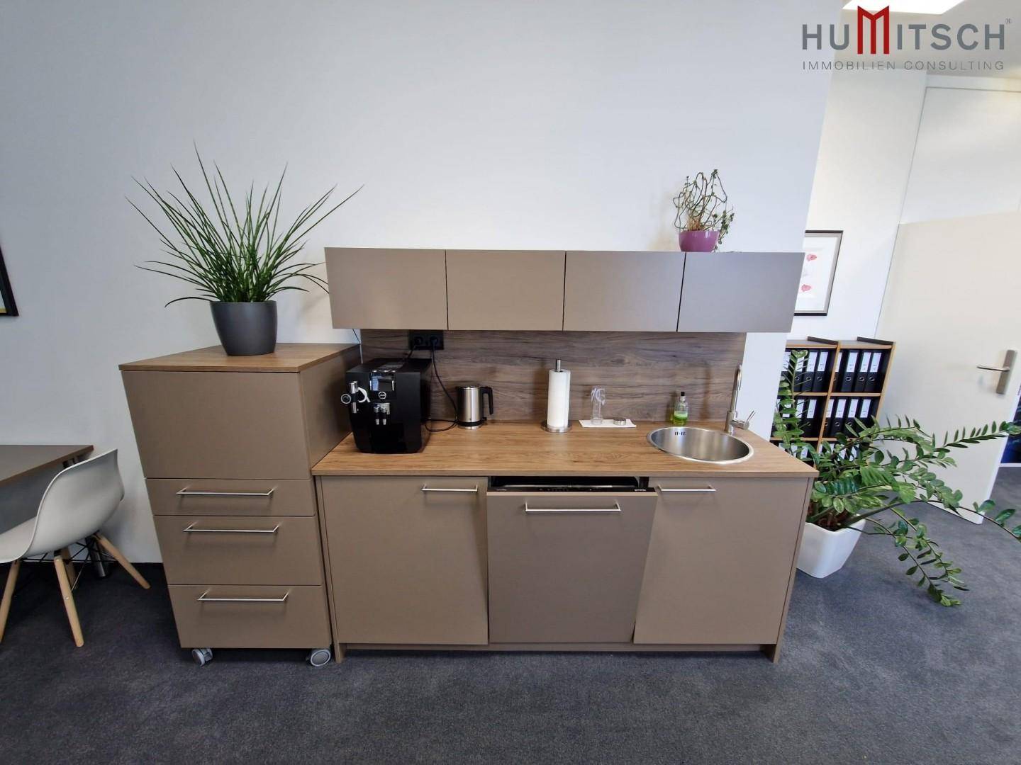 Kompakte Küchenzeile mit Spüle, Kaffeemaschine und Stauraum in einem Bürobereich.