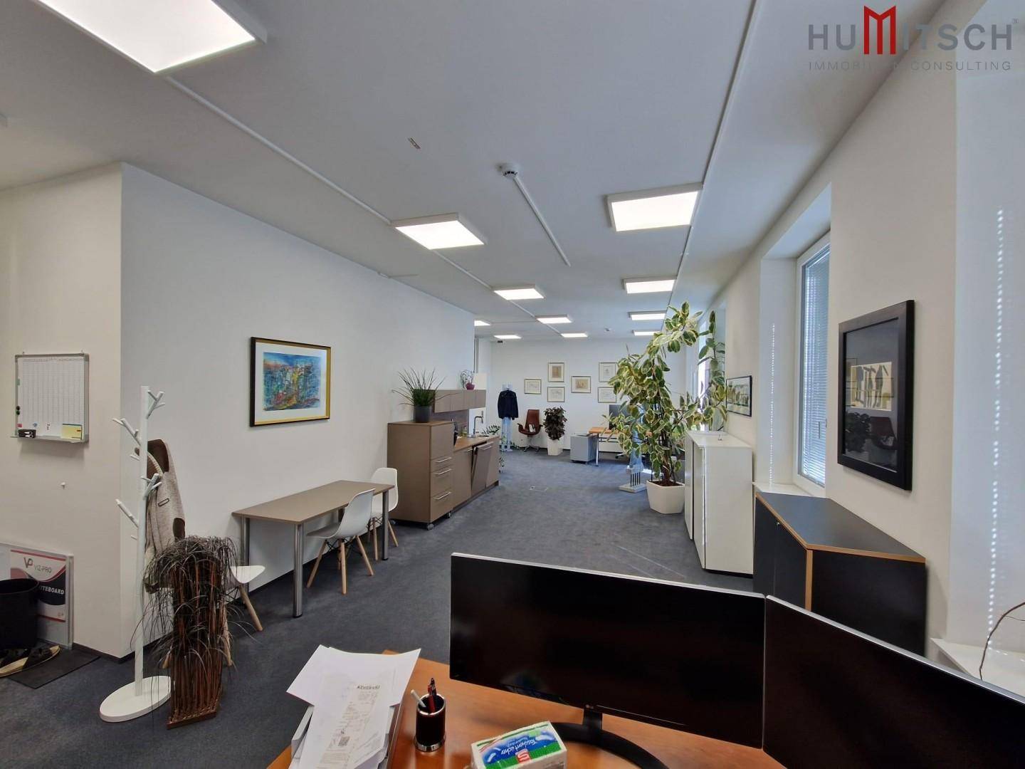 Heller Büroraum mit mehreren Arbeitsplätzen, Teppichboden und modernen Deckenleuchten.