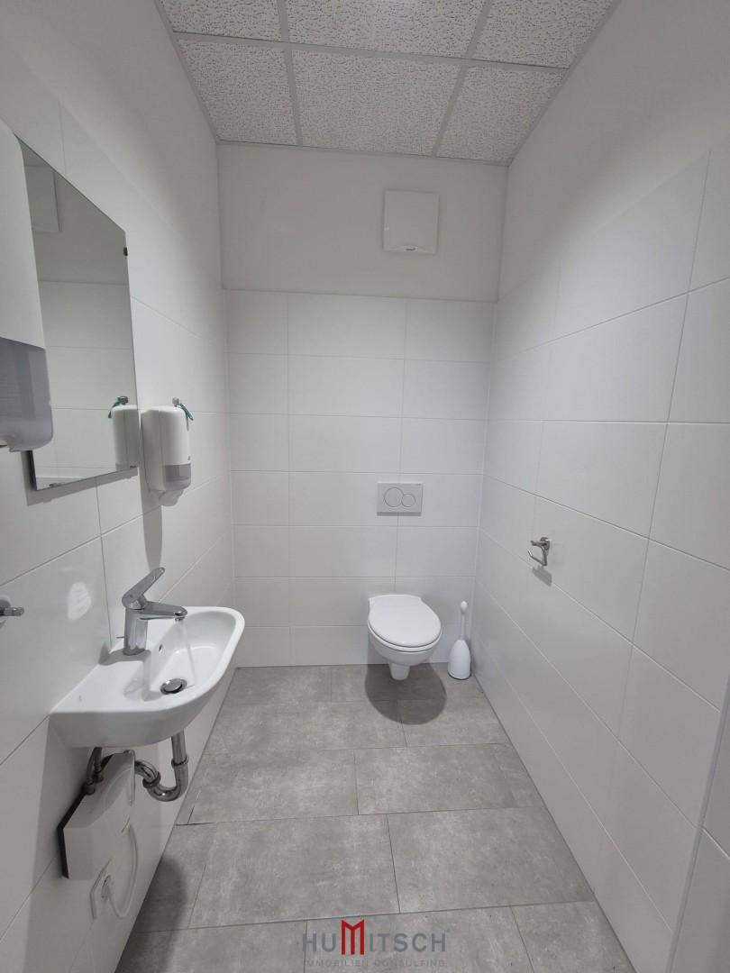 Modernes WC mit weißen Fliesen, einem Waschbecken und einer wandhängenden Toilette, in sehr gutem Zustand.