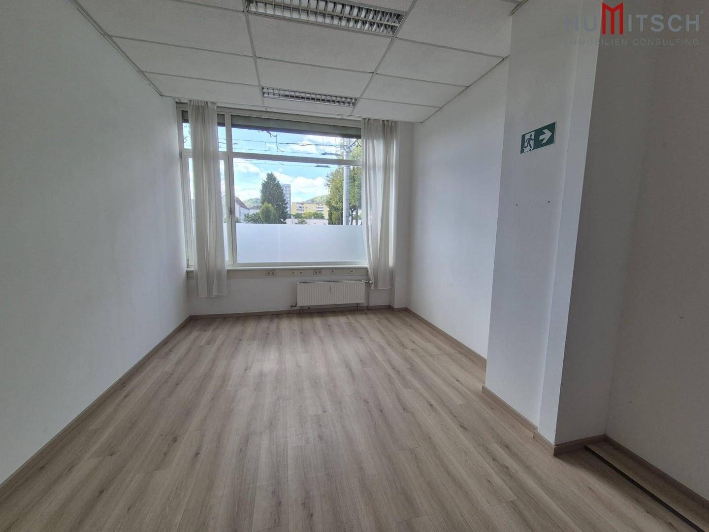 Kleiner, heller Büroraum mit Holzoptikboden, großen Fenstern und weißen Vorhängen, ideal für Einzelbüros.