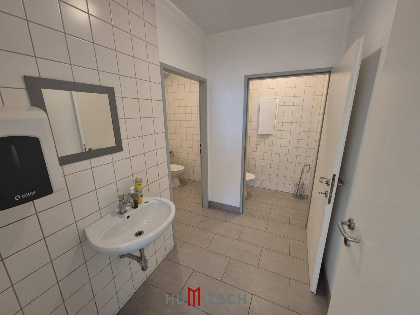Sanitärbereich mit zwei Toilettenkabinen, Waschbecken und gefliesten Wänden, in gutem Zustand.