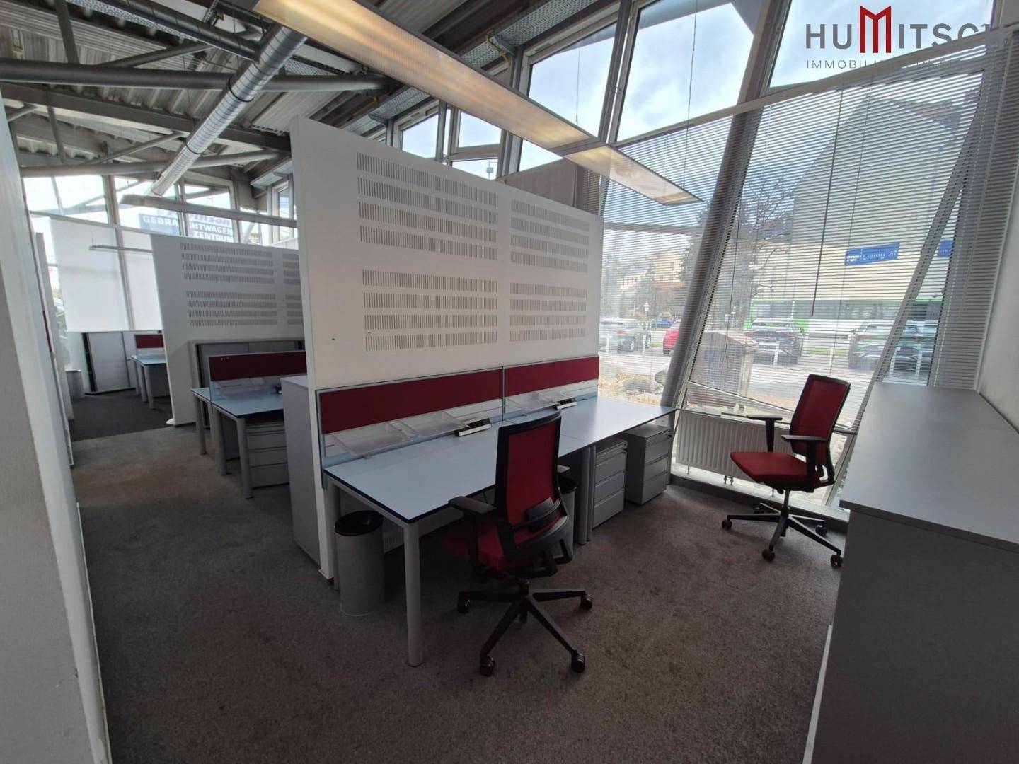 Moderner Bürobereich mit mehreren Arbeitsplätzen, Teppichboden und schrägen Glasfassaden, die viel Licht spenden.