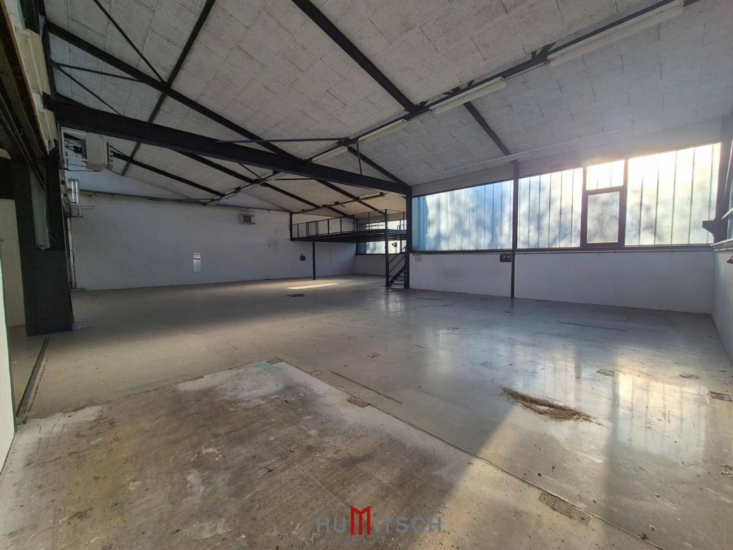 Geräumige Lagerhalle mit Betonboden, hohen Decken und einer erhöhten Plattform im Hintergrund.