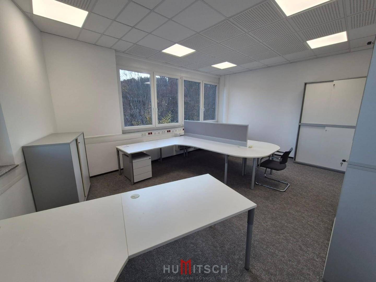 Geräumiges Büro mit Teppichboden, weißen Wänden und funktionalen Büromöbeln, bereit zur Nutzung.