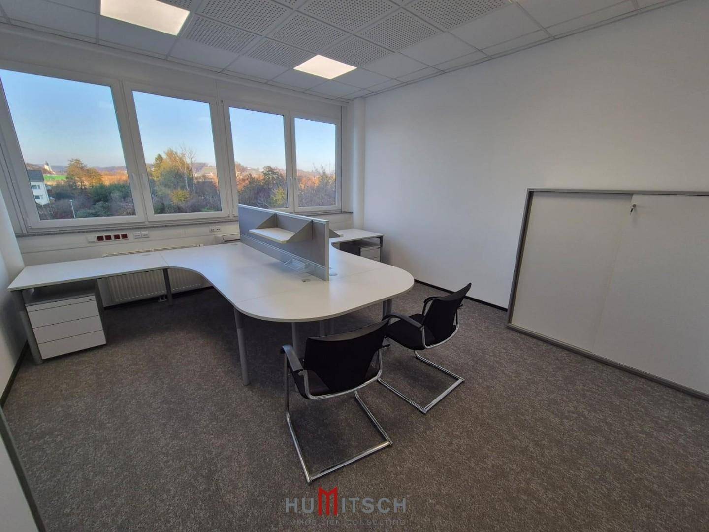 Helles Büro mit Teppichboden, ergonomischen Stühlen und einem Whiteboard für Präsentationen.