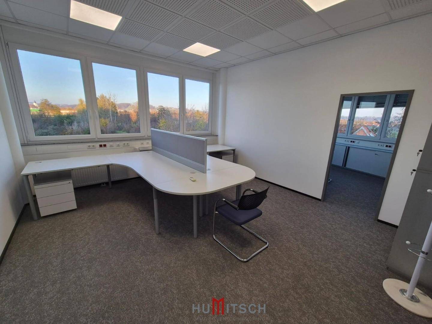 Büro mit Teppichboden und großen Fenstern, die viel Tageslicht hereinlassen und eine weite Aussicht bieten.