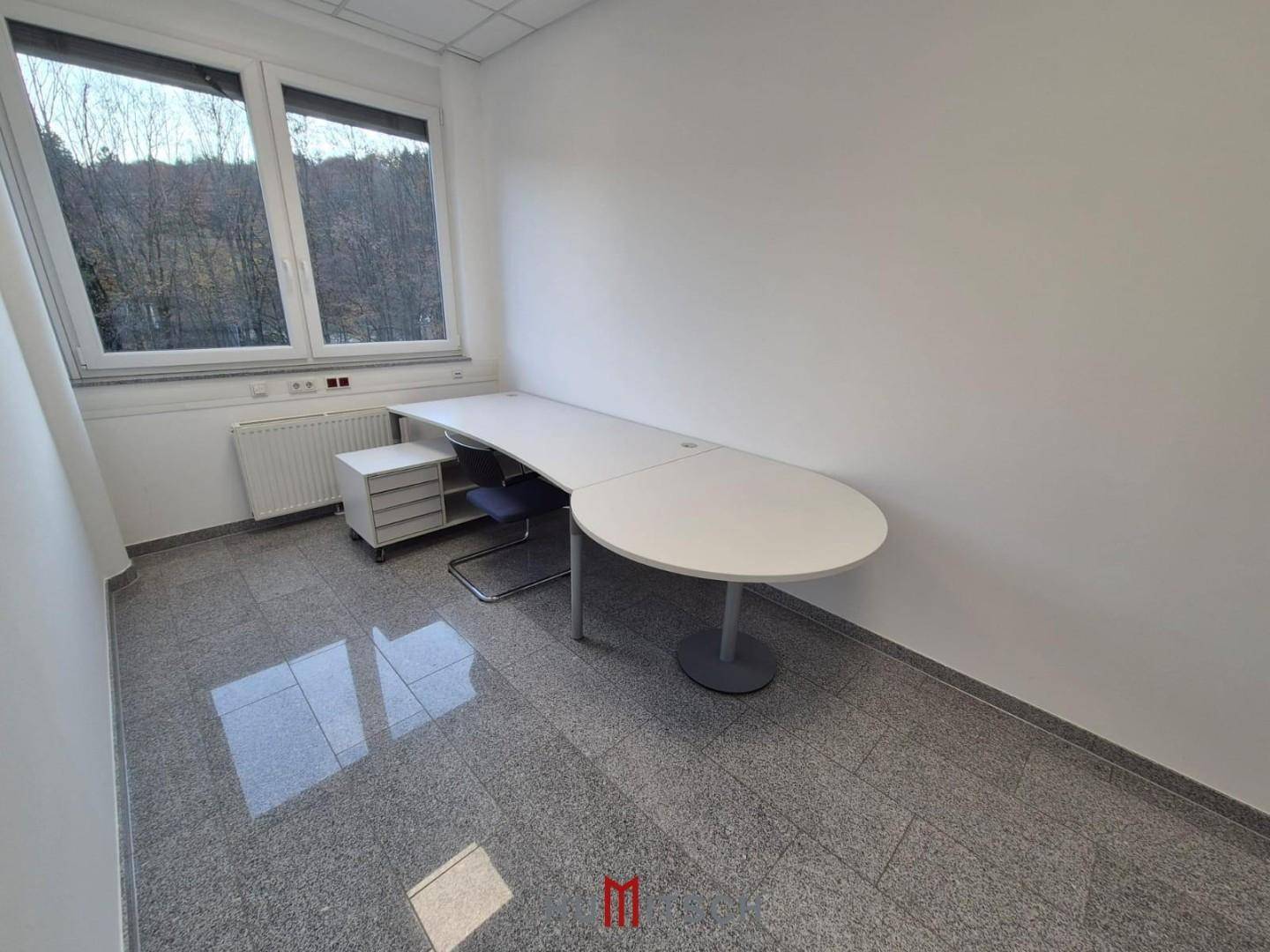 Einzelbüro mit Granitfliesenboden, einem langen Schreibtisch und Blick ins Grüne durch das Fenster.