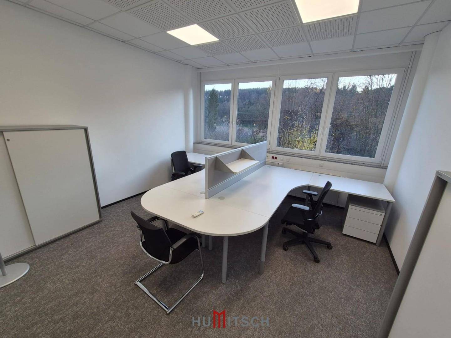 Helles Büro mit Teppichboden, mehreren Arbeitsplätzen und einem Whiteboard, ideal für Teamarbeit.