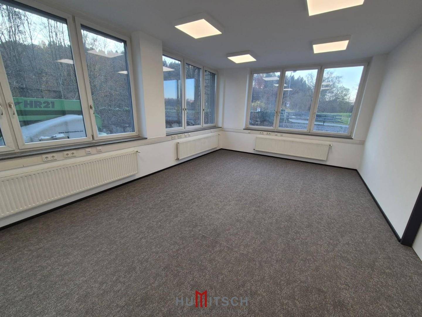 Großes Eckbüro mit vielen Fenstern, Teppichboden und Heizkörpern, bietet viel Tageslicht.