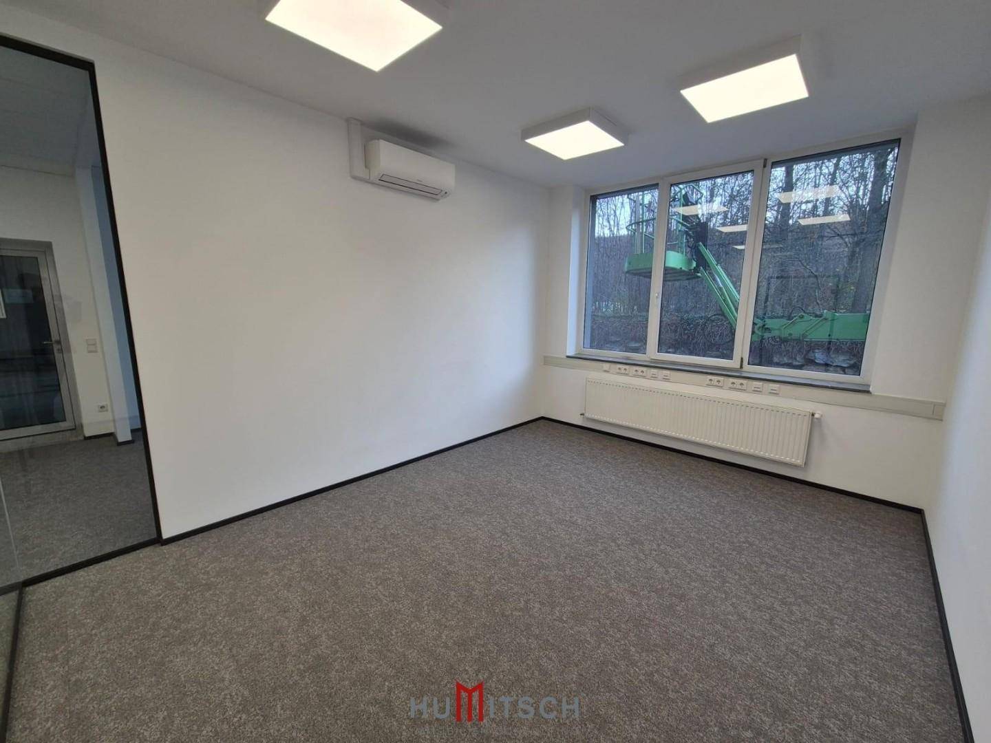 Helles Büro mit Teppichboden, großen Fenstern und Blick auf die Straße und umliegende Landschaft.