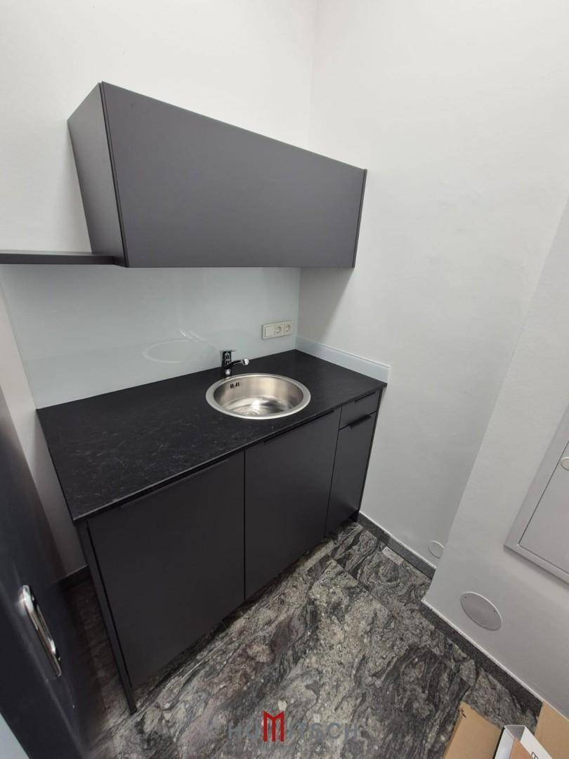 Kleine, moderne Teeküche mit Spülbecken, Unterschränken und Hängeschränken in Schwarz und Weiß.