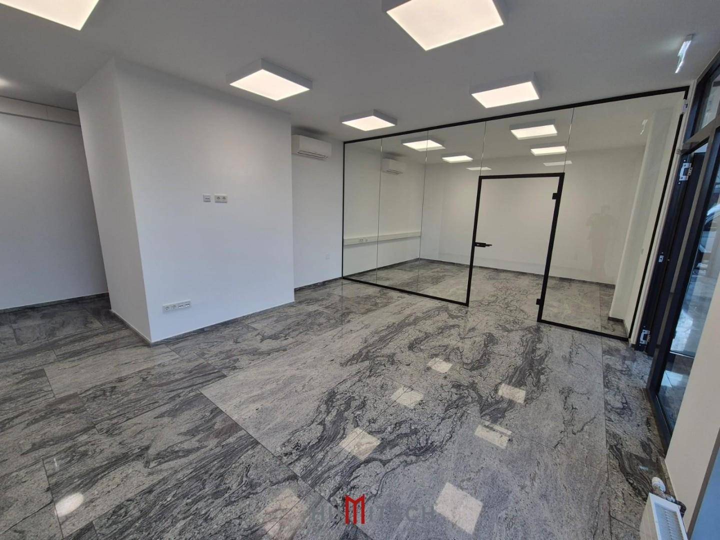 Modernes Büro mit Glaswänden zur Raumtrennung, Fliesenboden und Klimaanlage an der Wand.