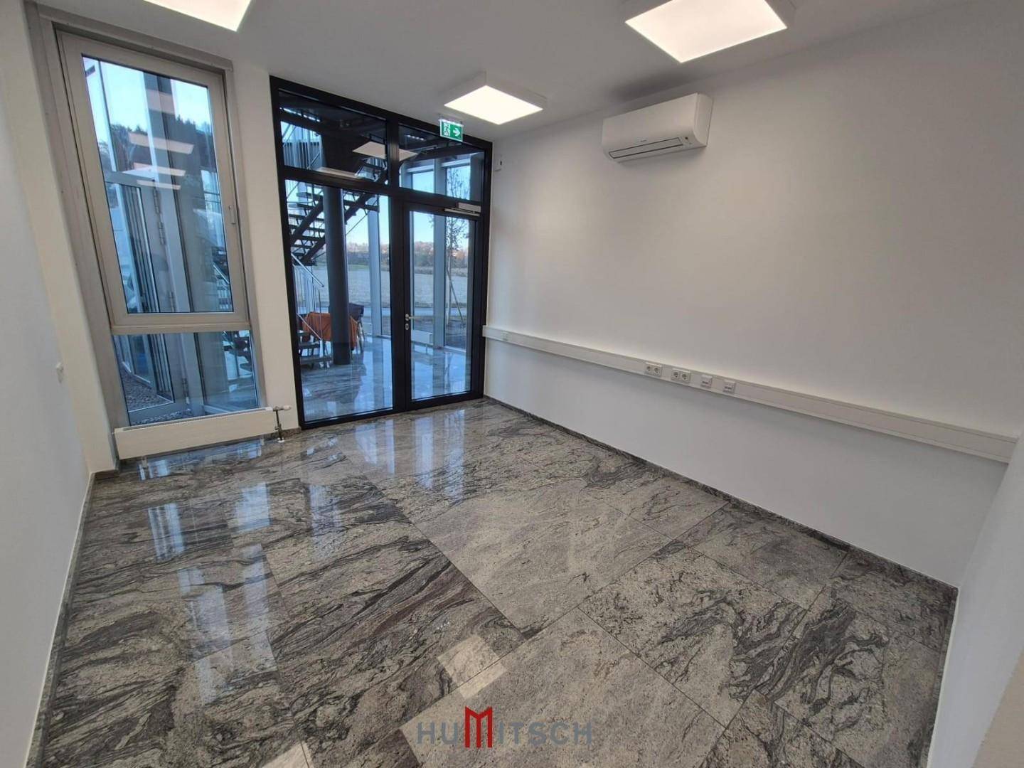 Büro mit großen Fenstern, die den Blick nach draußen freigeben, und einer Klimaanlage an der Wand.