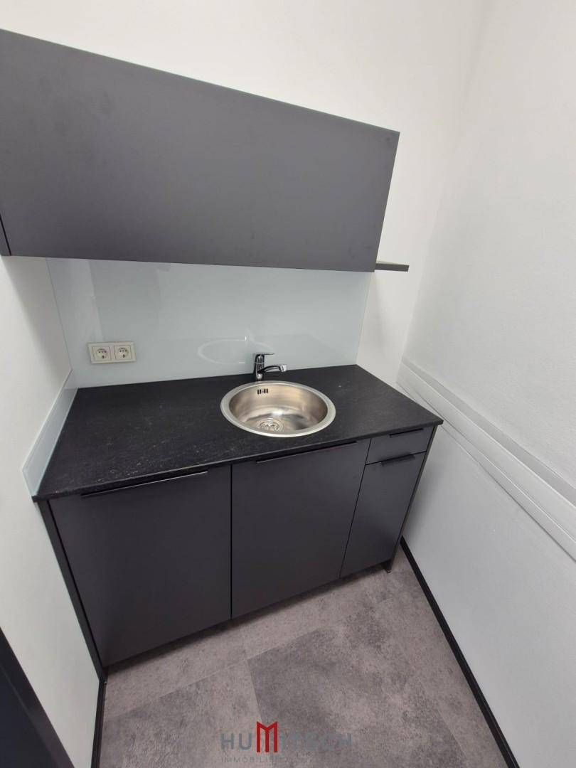 Moderne Küchenzeile mit dunklen Schränken, Spülbecken und Vinylboden, ideal für eine Büroküche.