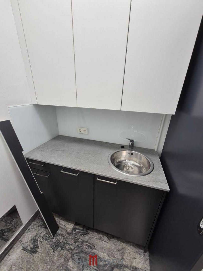 Kleine, moderne Teeküche mit Spülbecken, Unterschränken und Hängeschränken in Grau und Weiß.