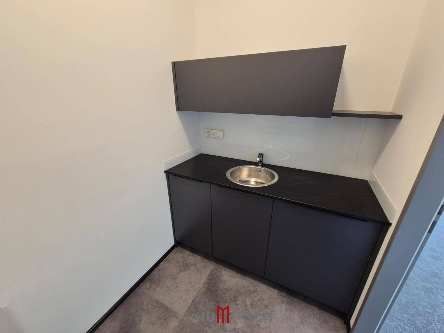 Moderne Küchenzeile mit dunklen Schränken, Spülbecken und Vinylboden, ideal für eine Büroküche.