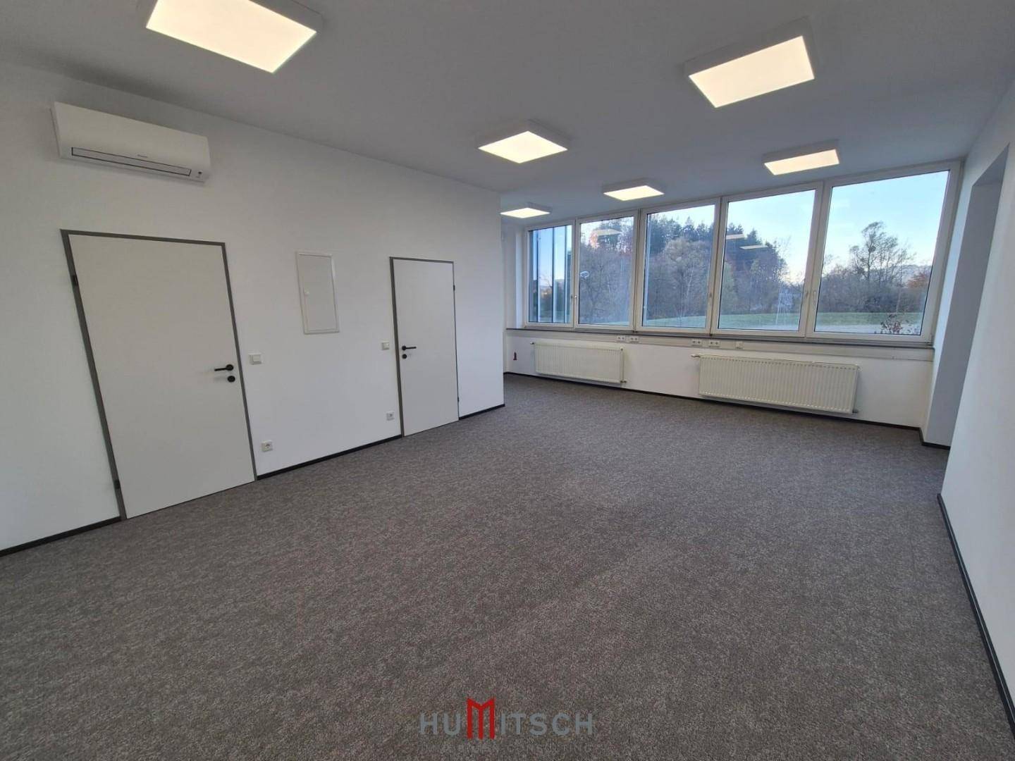 Helles Büro mit Teppichboden, großen Fenstern und Klimaanlage, bietet einen weiten Ausblick.