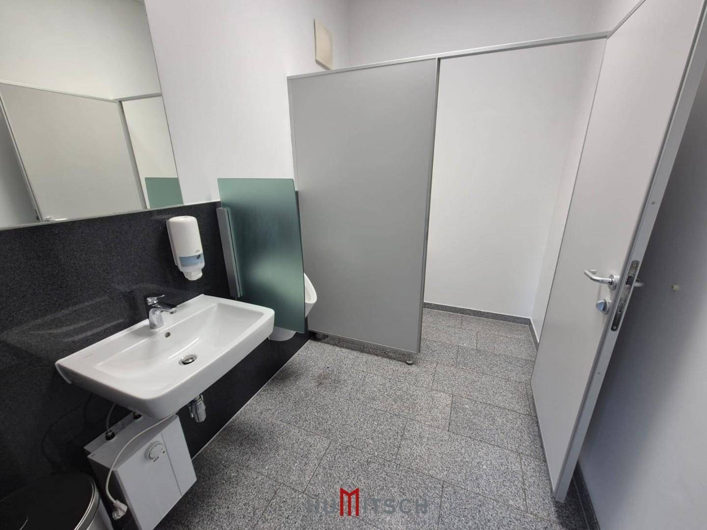 Moderne Toilette mit Waschbecken, Spiegel und Granitboden, inklusive Urinal und Trennwänden.
