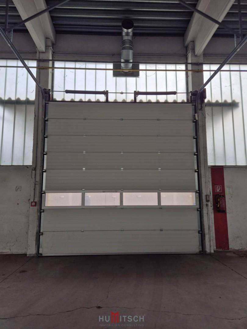 Großes Sektionaltor von innen in einer Industriehalle, mit kleinen Fenstern im unteren Bereich für etwas Lichteinfall.
