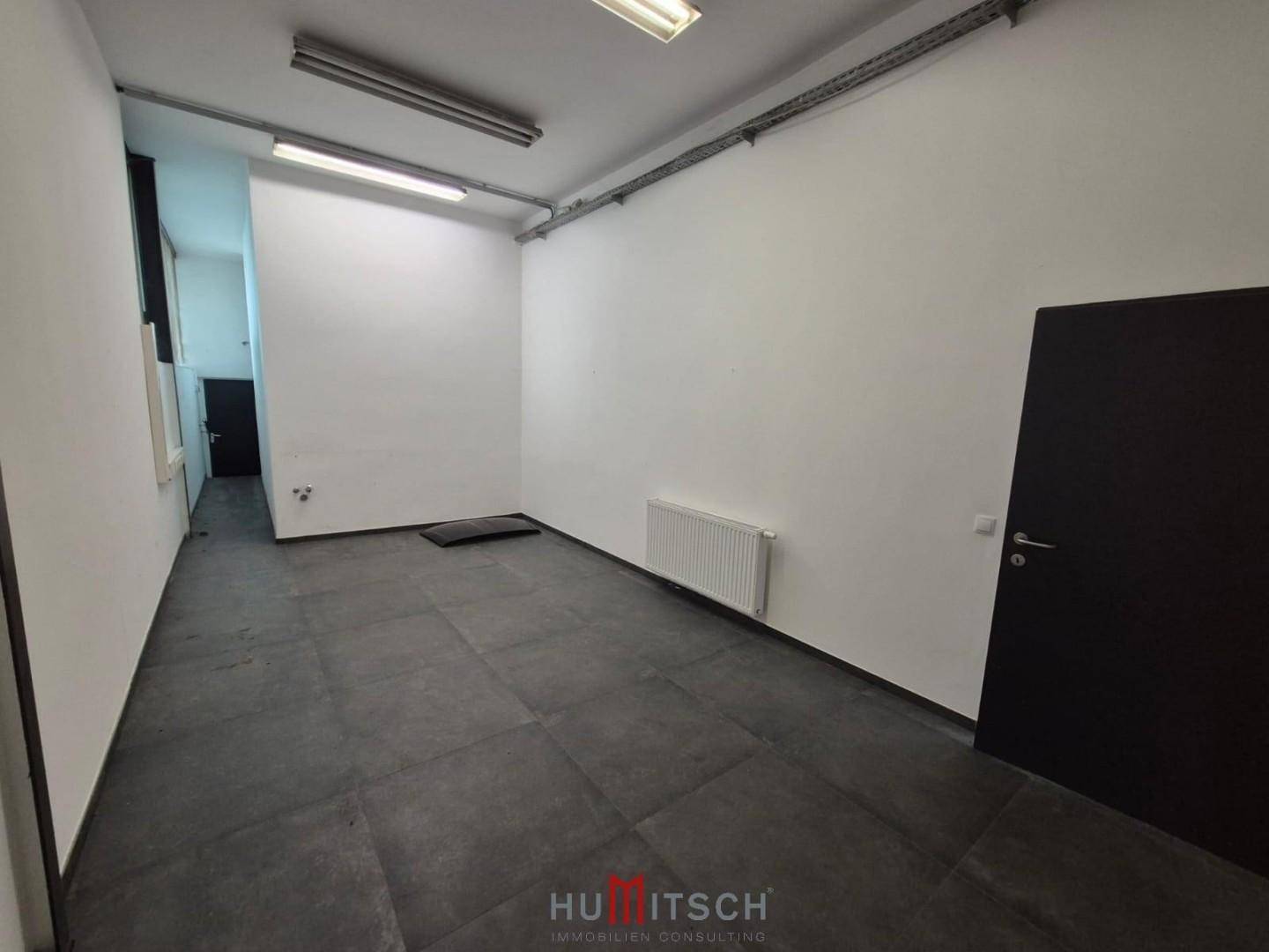 Kleiner, sauberer Raum mit weißen Wänden, dunklem Fliesenboden und einem Heizkörper unter dem Fenster.