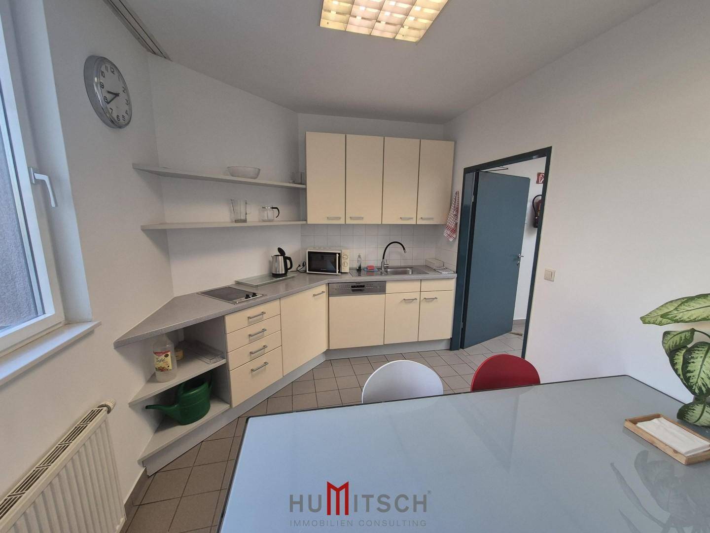 Funktionale Küchenzeile mit hellen Schränken, Spüle, Kochfeld und Mikrowelle, ideal für Büronutzung.