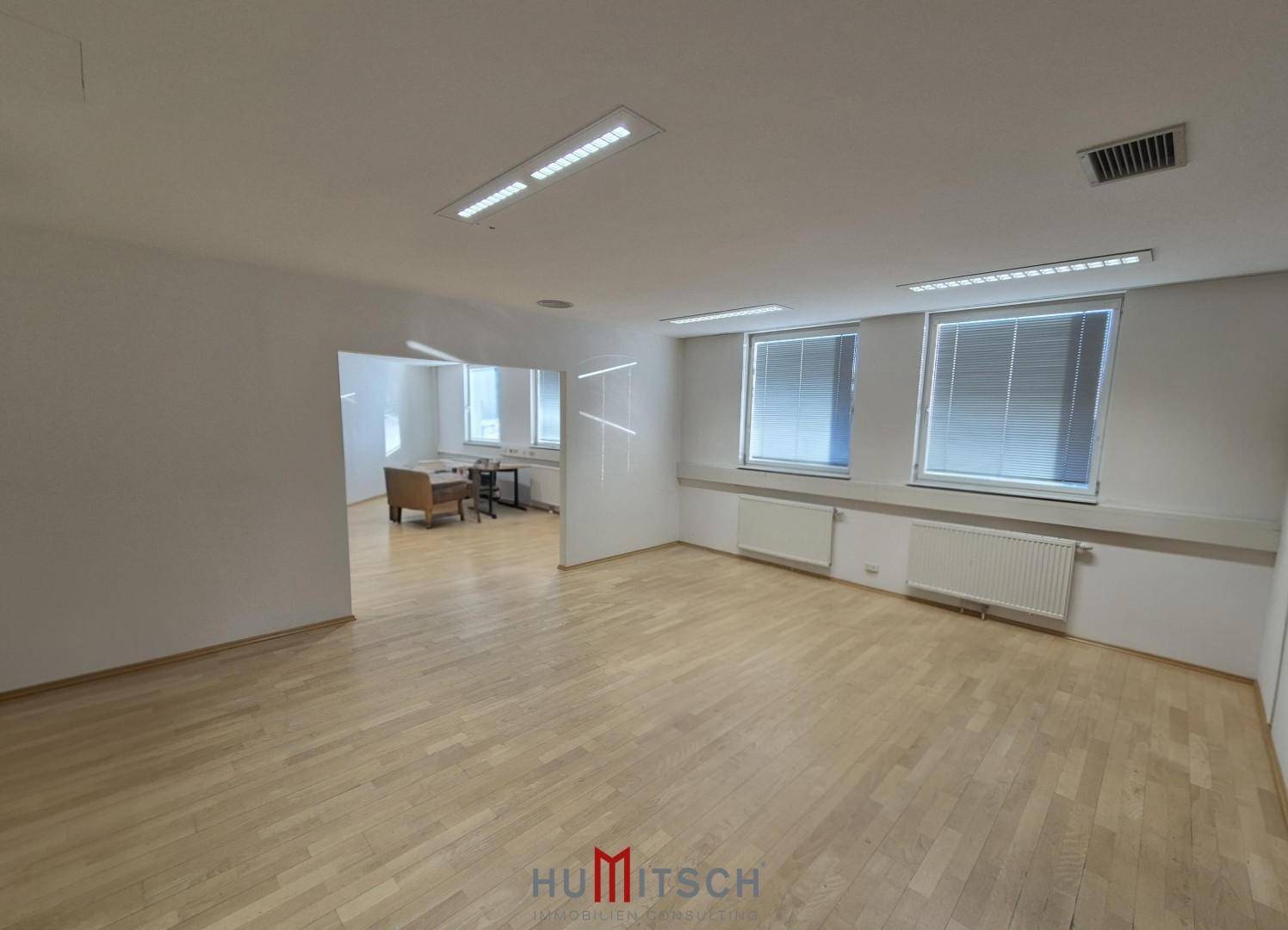 Helles Büro mit Parkettboden und mehreren Fenstern, die viel Tageslicht hereinlassen, ideal für flexible Nutzung.