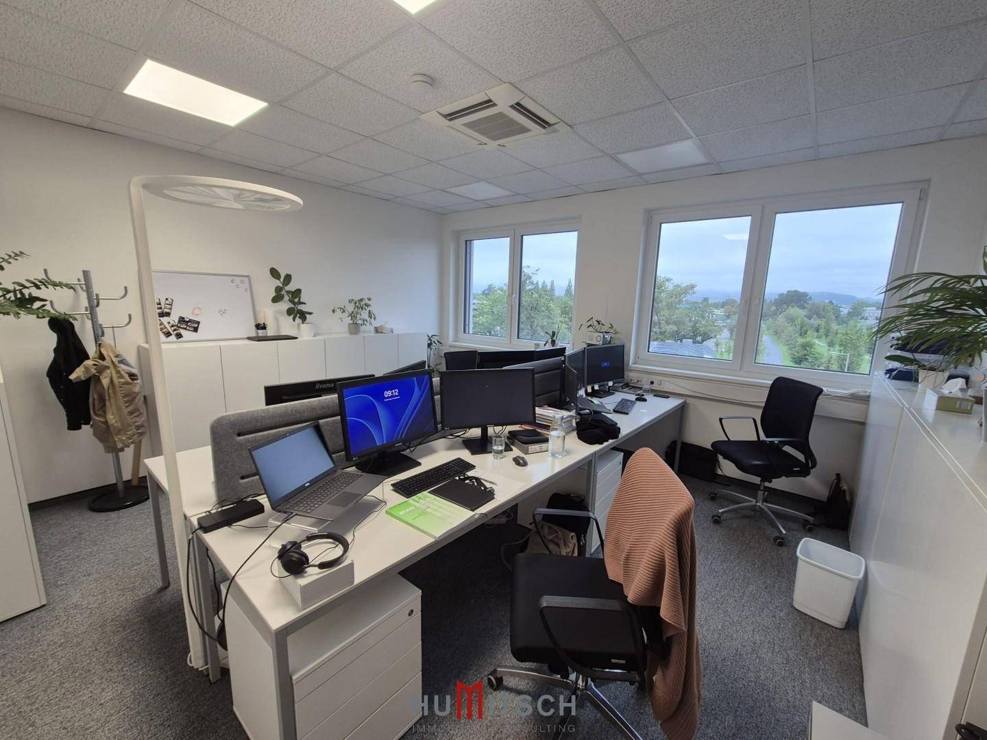 Helles Büro mit mehreren Arbeitsplätzen, ergonomischen Stühlen und Blick auf die Landschaft.