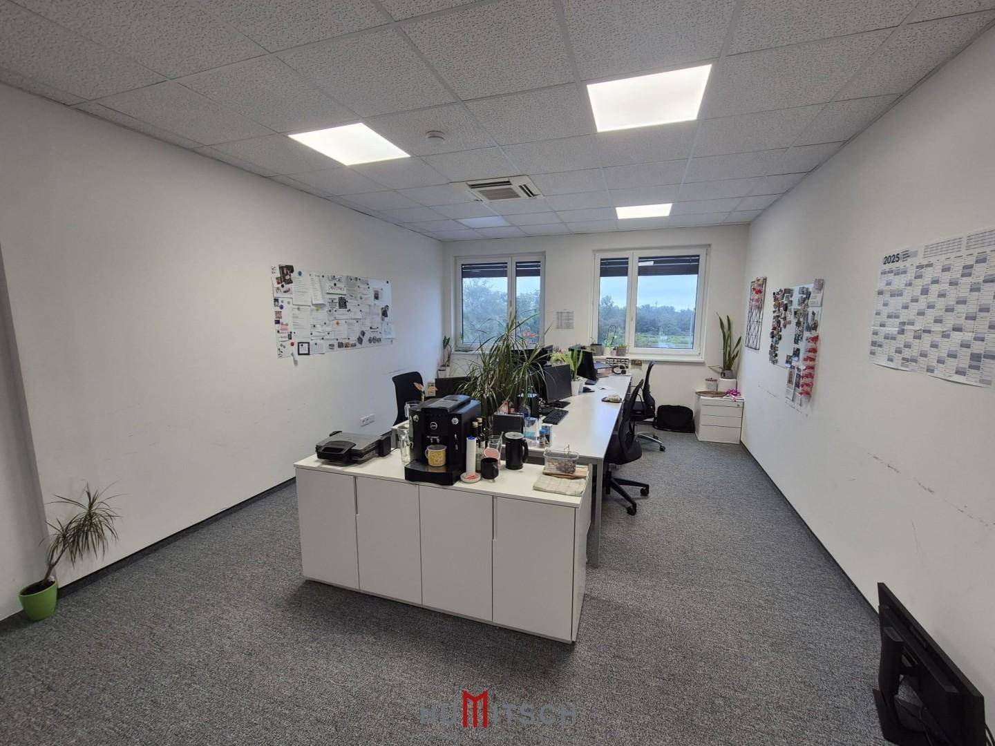 Geräumiges Großraumbüro mit mehreren Arbeitsplätzen, Teppichboden und großen Fenstern für viel Tageslicht.