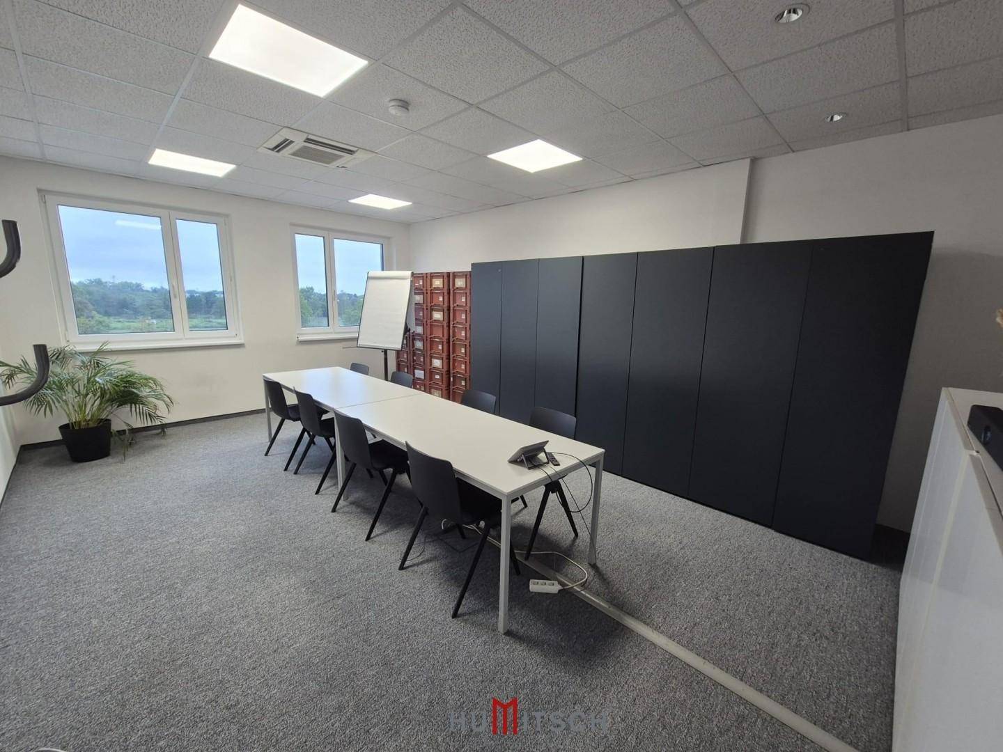 Konferenzraum mit einem langen Tisch, schwarzen Stühlen und einer großen schwarzen Schrankwand.