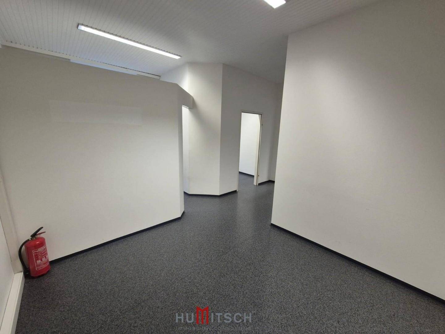 Heller Flurbereich mit grauem Boden, weißen Wänden und mehreren Türen, inklusive Feuerlöscher.