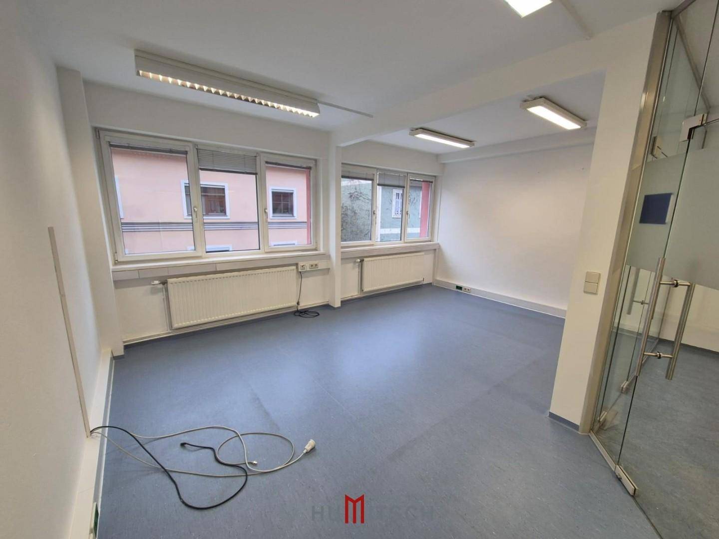 Helles Büro mit mehreren Fenstern, grauem Boden und weißen Wänden, bereit zur Einrichtung.