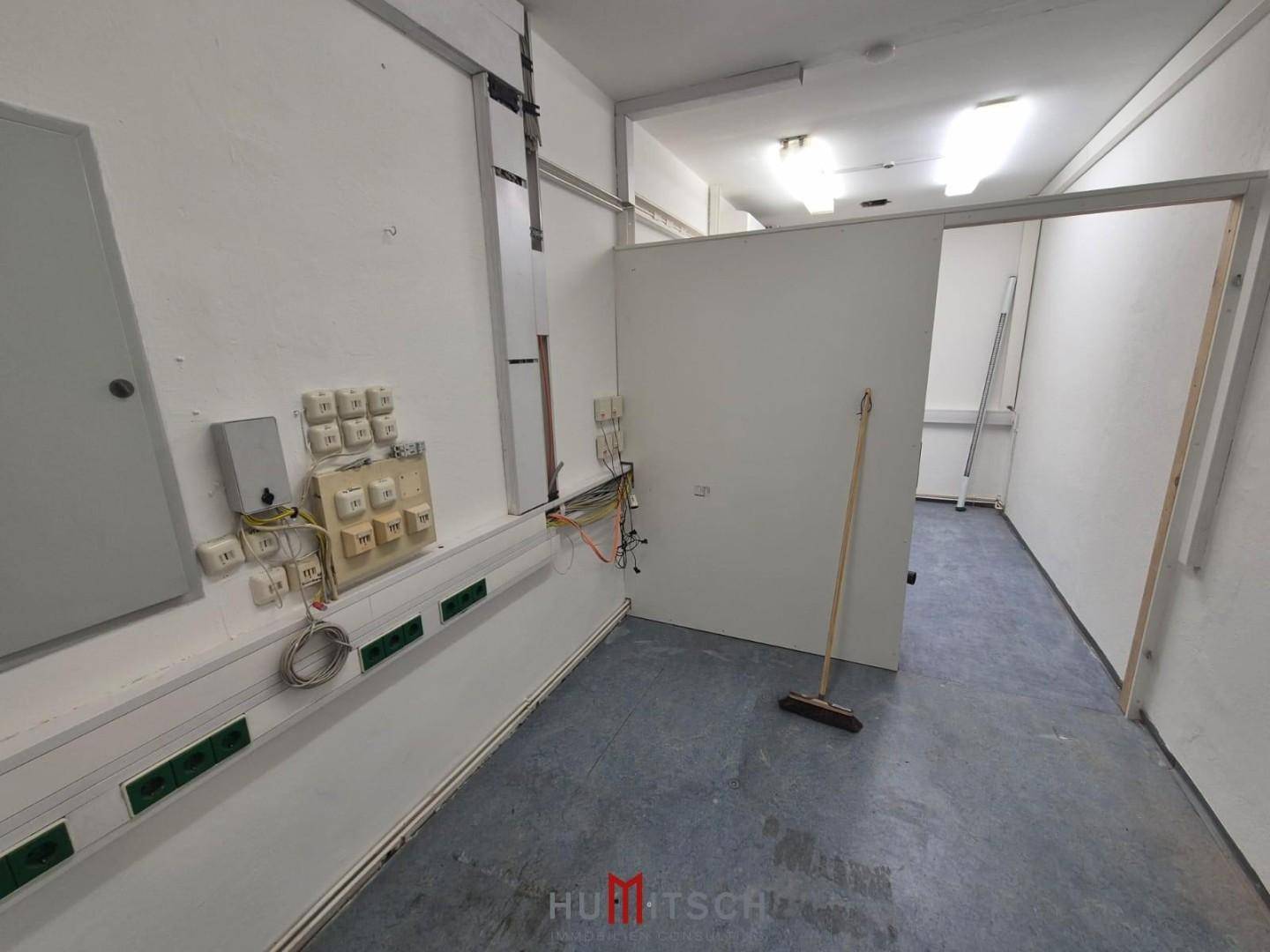 Technikraum mit sichtbaren Kabeln, einer Trennwand und grauem Bodenbelag.