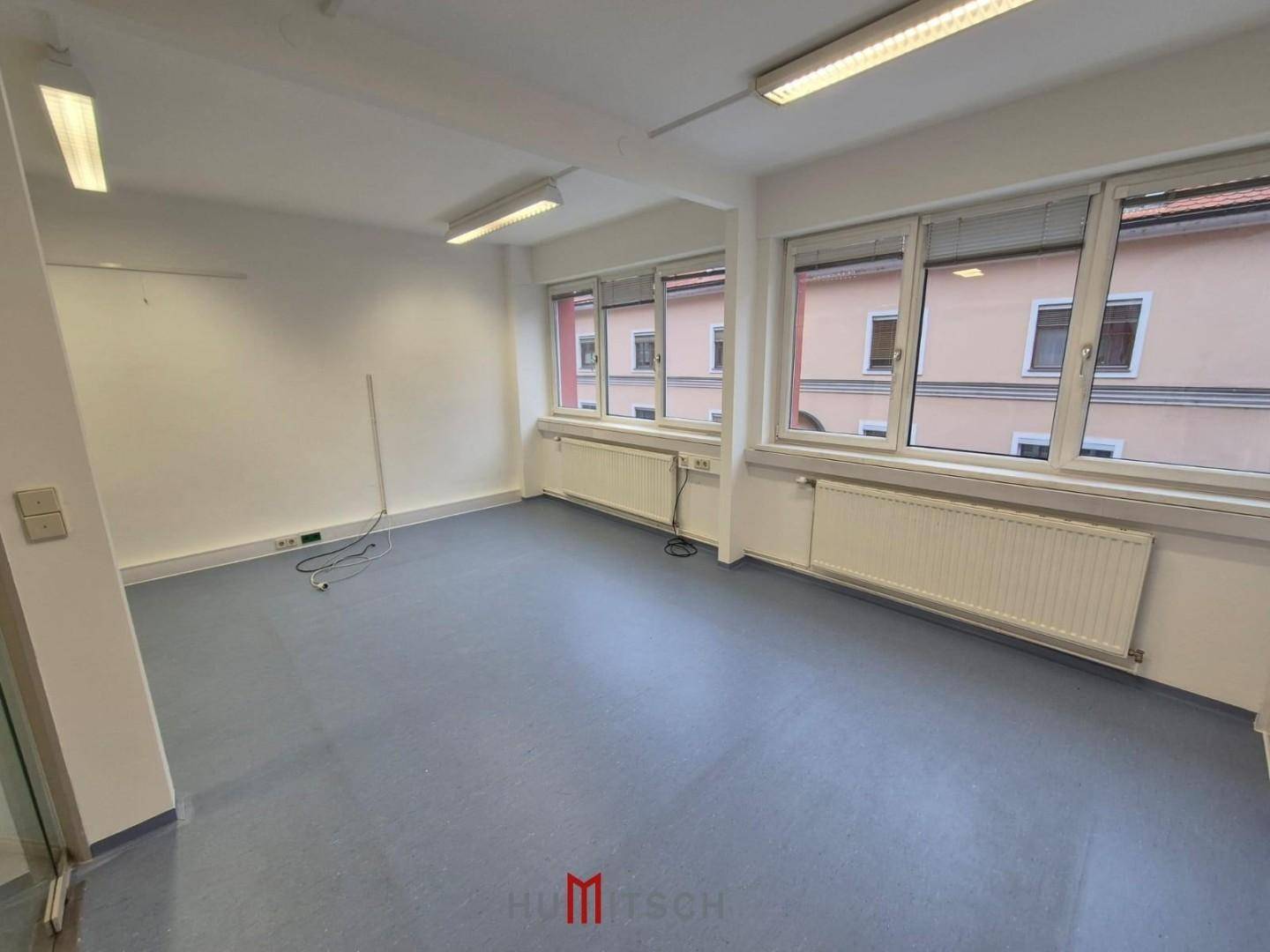 Leeres Büro mit großen Fenstern, die viel Tageslicht hereinlassen, und grauem Vinylboden.