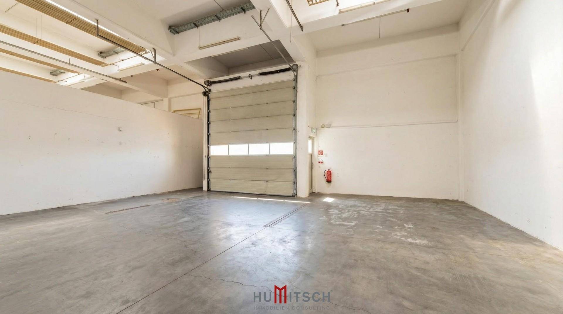 Leere Lagerhalle mit großem Rolltor und Betonboden, ideal für Logistik oder Produktion.