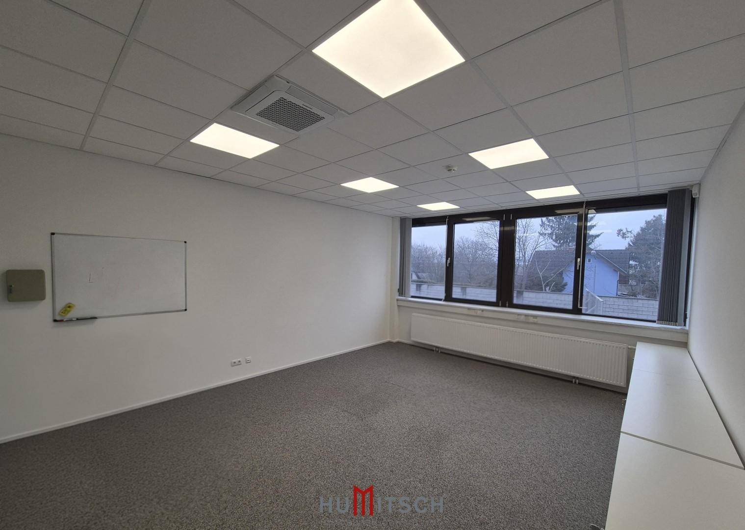 Heller Büroraum mit Teppichboden, Fensterfront und einer Wandtafel, bereit zur Nutzung.