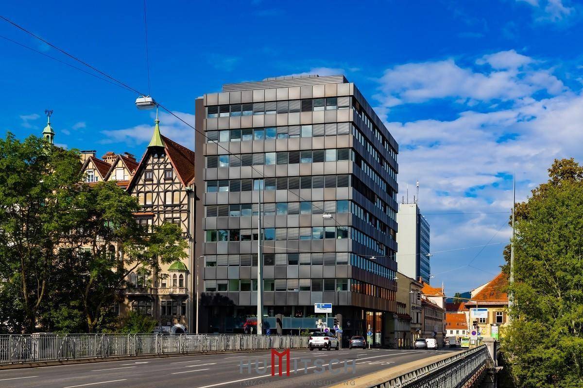 Ansicht eines modernen Geschäftsgebäudes mit vielen Fenstern und einer belebten Straße im Vordergrund.
