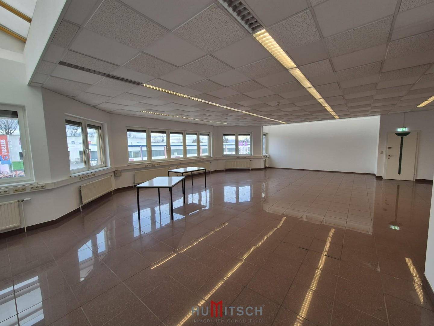 Weitläufiger Bürobereich mit glänzenden Fliesen, vielen Fenstern und einer modernen Deckenbeleuchtung.