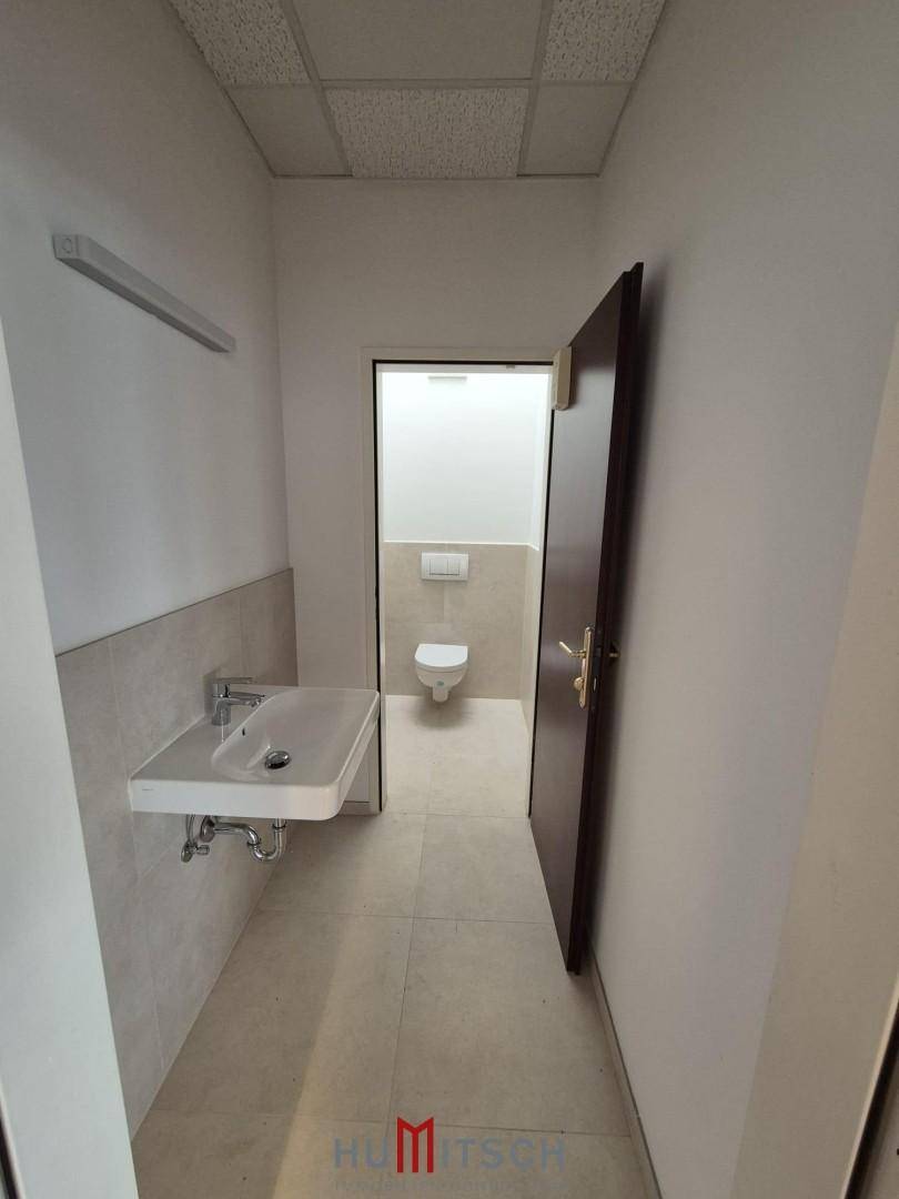 Sauberer Sanitärbereich mit modernem Waschbecken, Wand-WC und hellen Fliesen an Wänden und Boden.