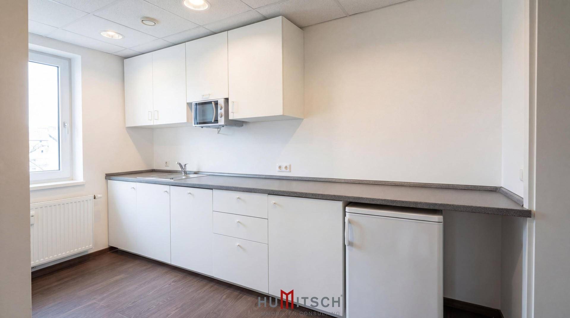 Funktionale Küchenzeile mit weißen Schränken, Spüle, Mikrowelle und Kühlschrank in einem hellen Raum.