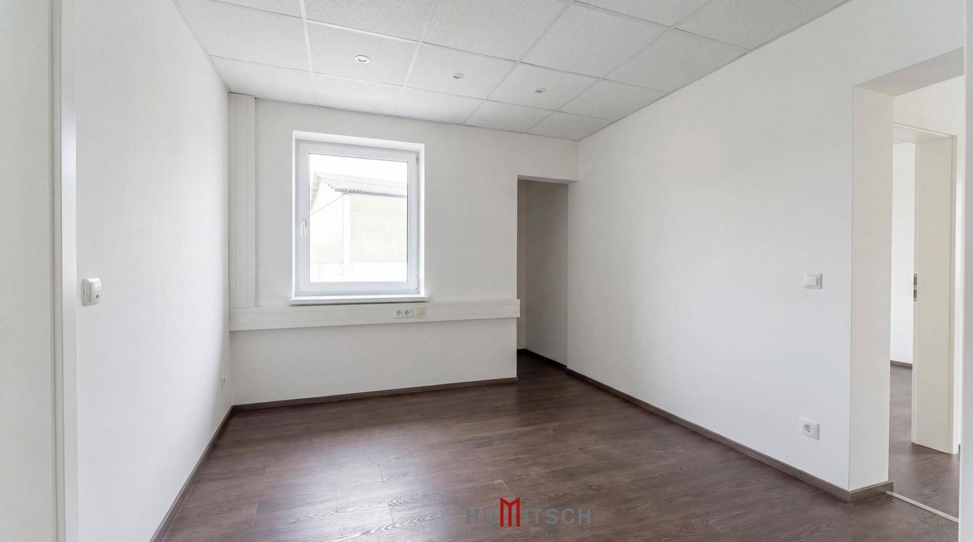 Heller Büroraum mit Laminatboden, weißen Wänden und einem Fenster, bereit zur individuellen Gestaltung.