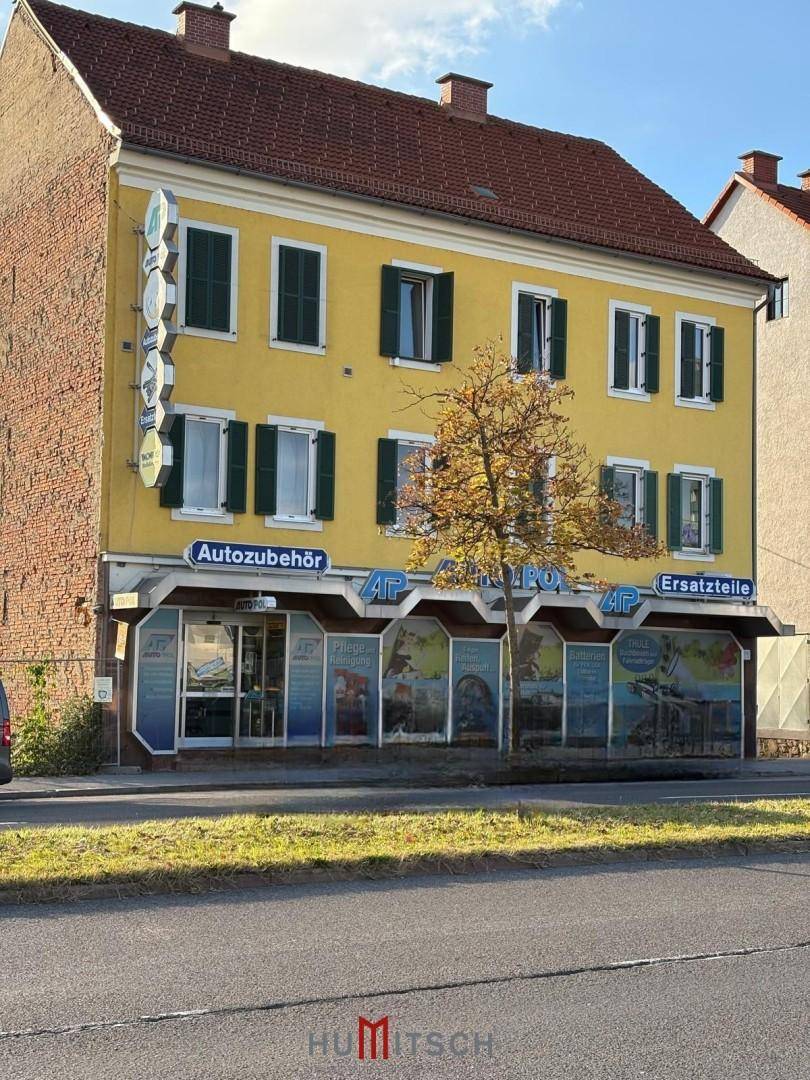 Vorderansicht eines gelben Gebäudes mit grünen Fensterläden und Geschäftsflächen im Erdgeschoss.