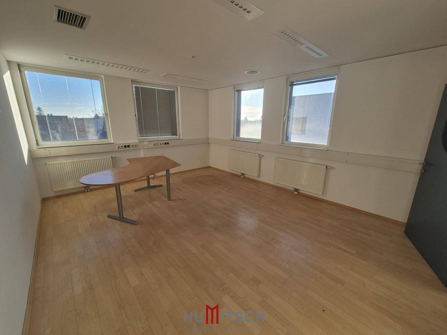 Helles Büro mit Holzfußboden, mehreren Fenstern und Heizkörpern, ideal für gewerbliche Nutzung.