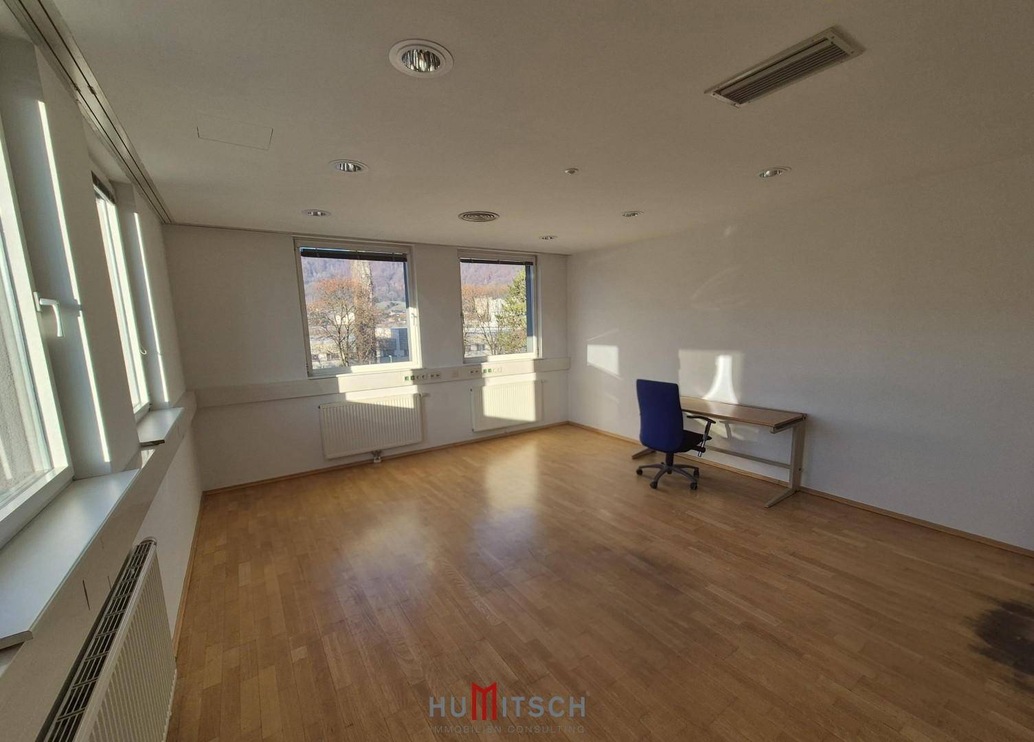 Geräumiges Büro mit viel Tageslicht, Holzparkett und einem Arbeitsplatz, bereit zur Einrichtung.