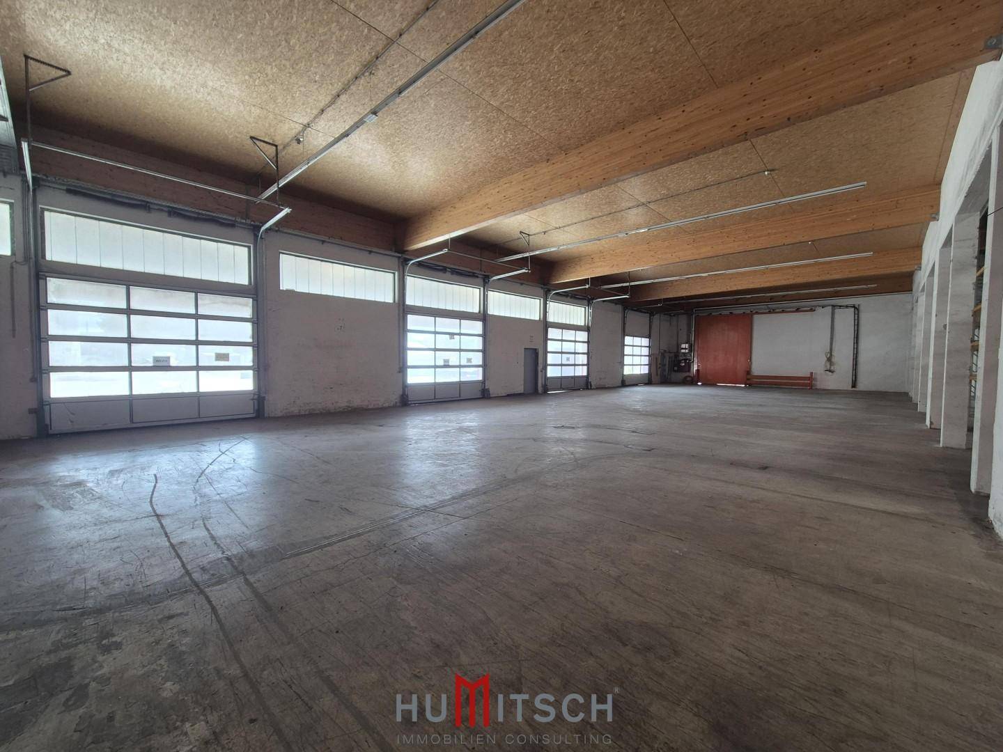 Große Lagerhalle mit mehreren Rolltoren, Holzdachkonstruktion und Betonboden.