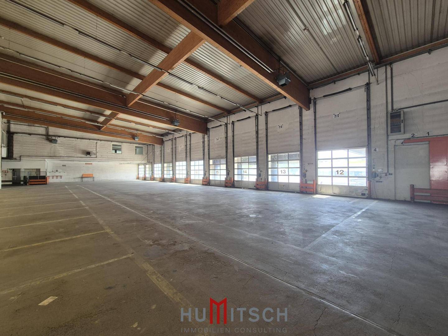 Lange Lagerhalle mit zahlreichen Rolltoren entlang einer Wand und Betonboden.