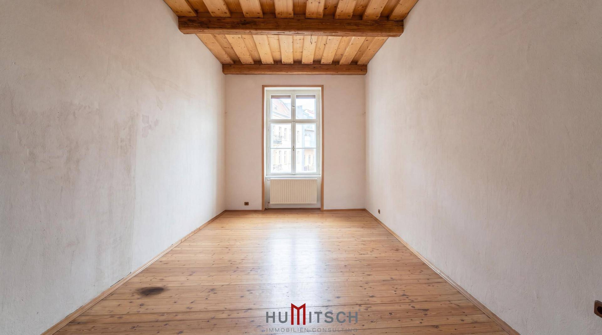 Gemütliches Zimmer mit Holzdielenboden, weißen Wänden und sichtbaren Deckenbalken.