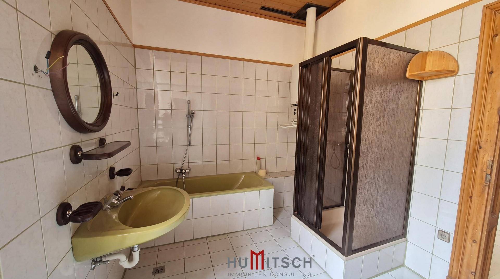 Badezimmer im Stil der 80er Jahre mit grüner Badewanne, Waschbecken und Duschkabine.