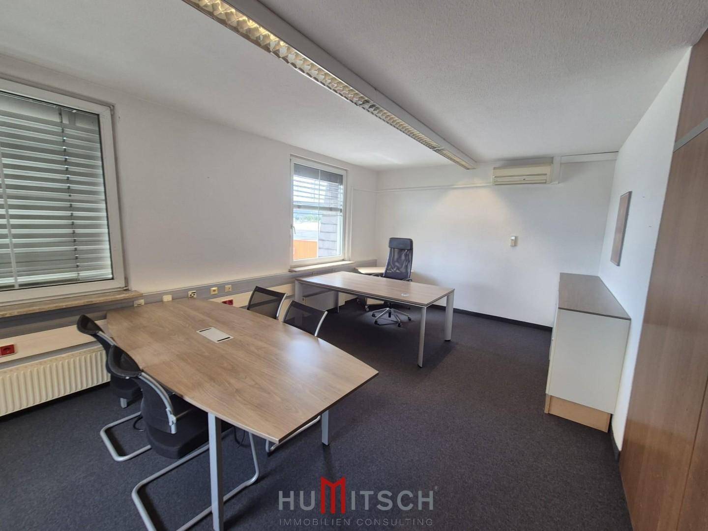 Büro mit Teppichboden, einem großen Besprechungstisch und einem einzelnen Schreibtisch.